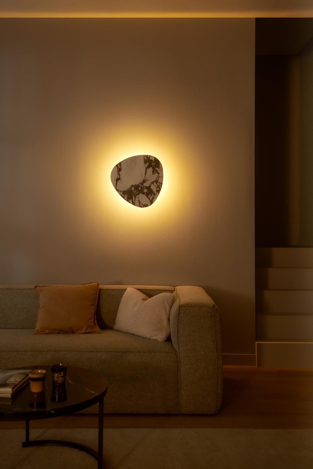 Woonkamer bij avond, verlicht door een wandlamp in marmer